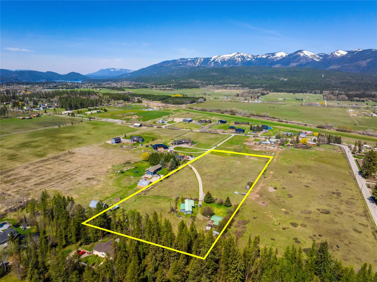 Aerial view of a large grassy lot outlined in yellow, with mountains and trees in the background.