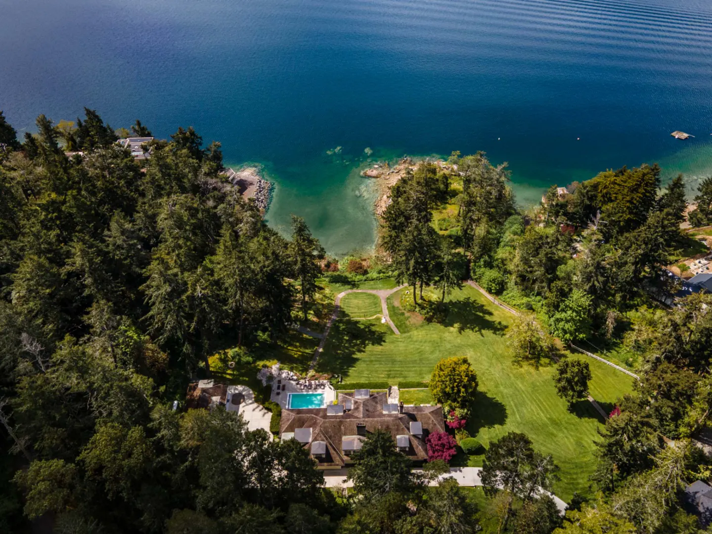 Aerial view of a luxury home with a pool, nestled among green trees near a blue lake.
