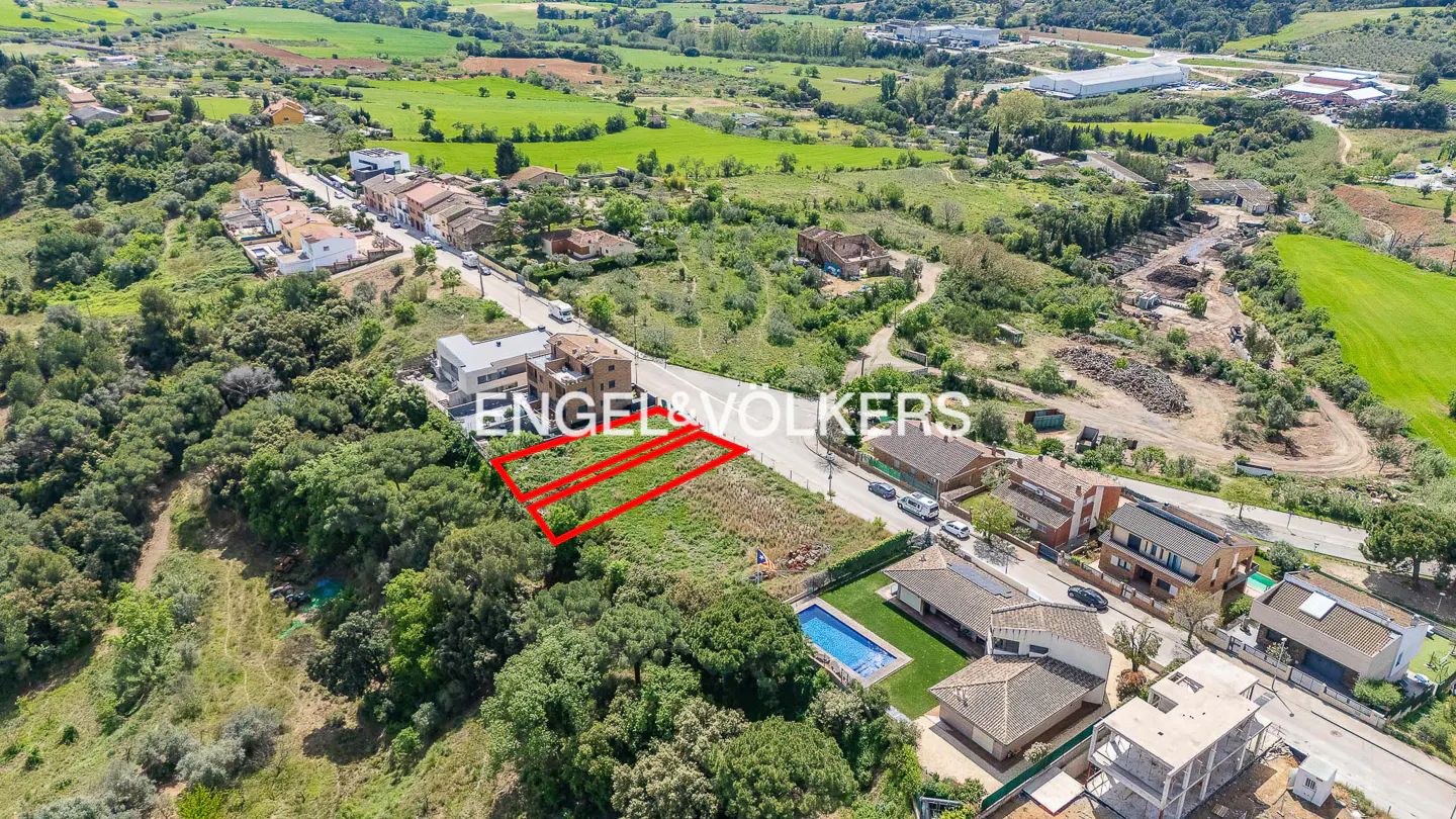 Aerial view of two adjacent plots of land outlined in red, near a road with houses and trees. Engel & Volkers logo visible.