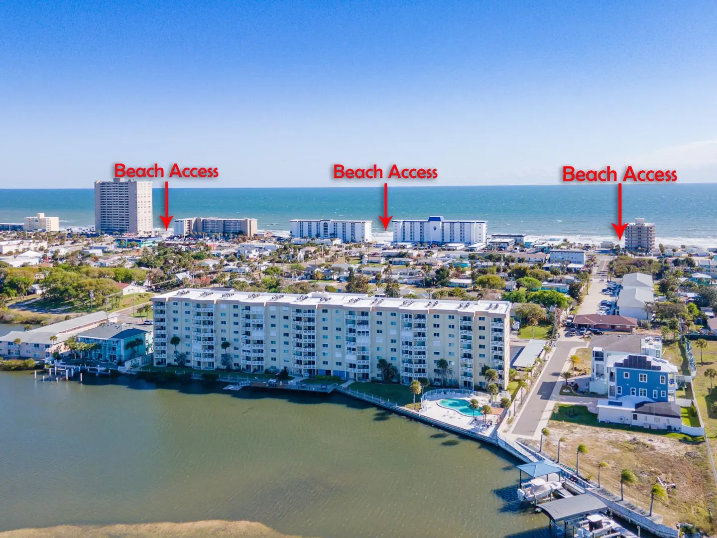 Aerial view of a condo complex with beach access, a pool, and a boat dock on a sunny day.