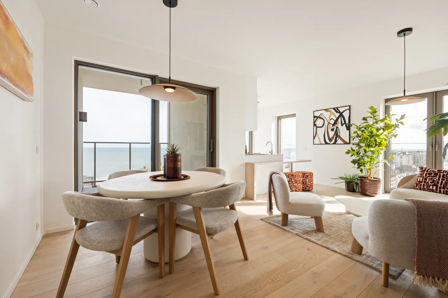 Modern dining and living area with light wood floors, a round table, textured chairs, and a view of the ocean.