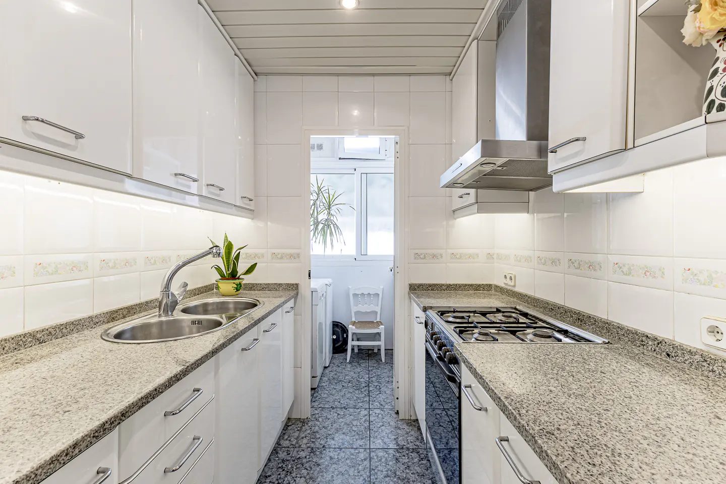 A galley kitchen with white cabinets, granite countertops, stainless steel appliances, and a view to a laundry area.