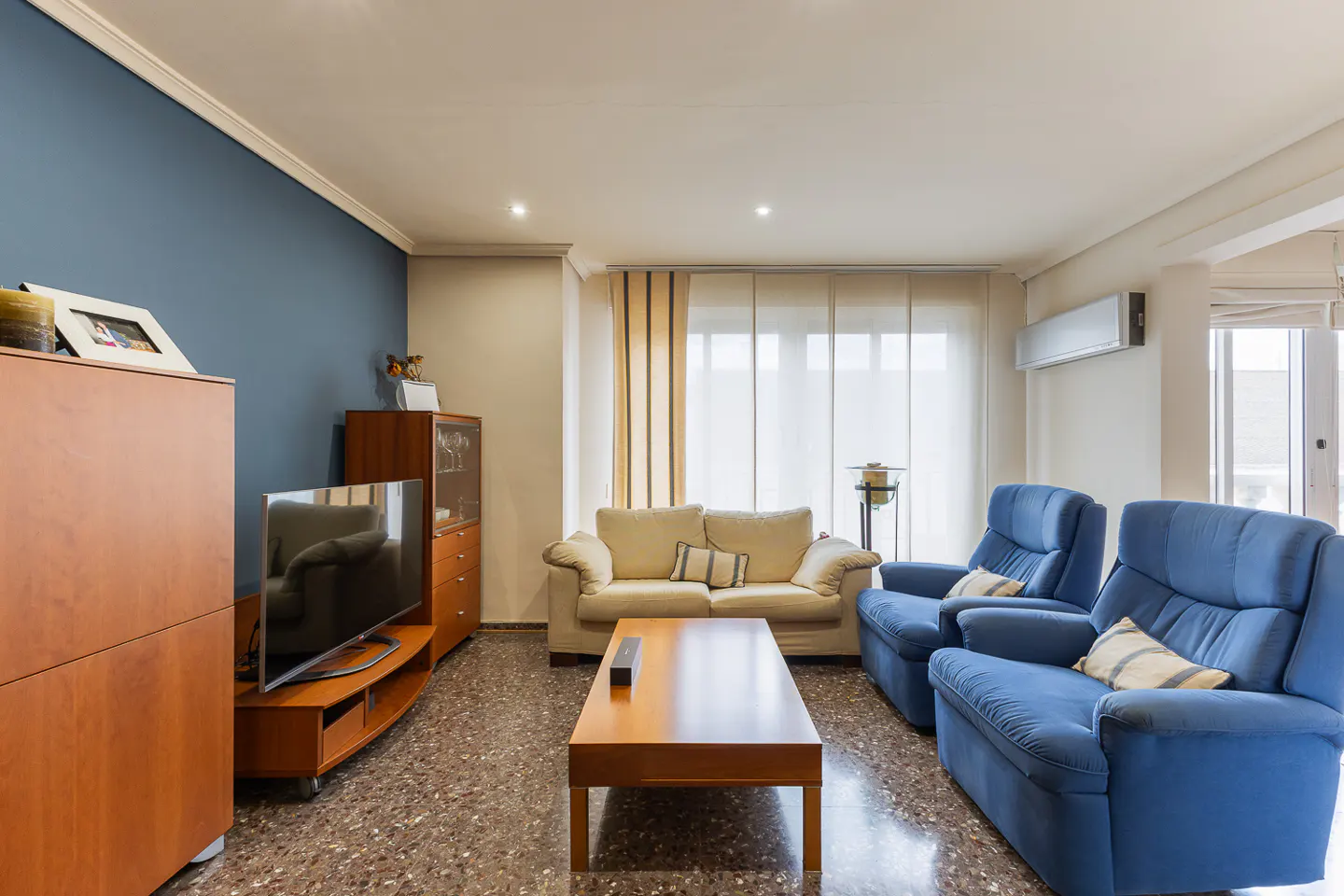 Living room with blue accent wall, wood furniture, beige sofa, and two blue armchairs. A wood coffee table sits in the center.