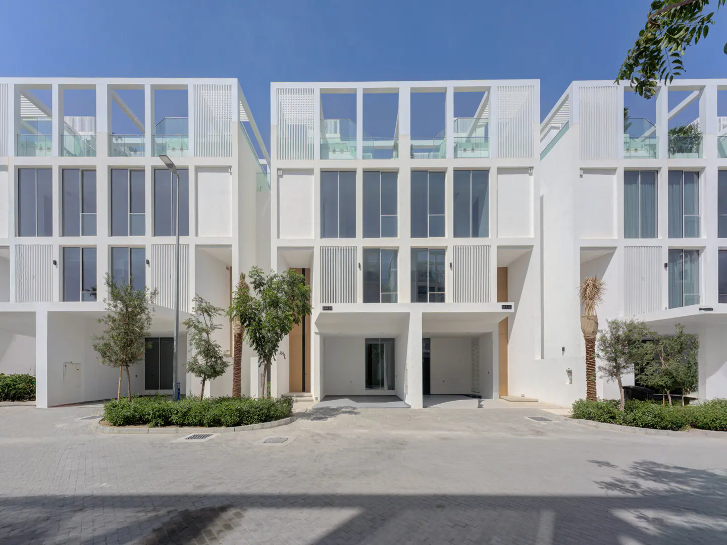 Modern, three-story white townhouses with large windows and open-air rooftop terraces under a clear blue sky.