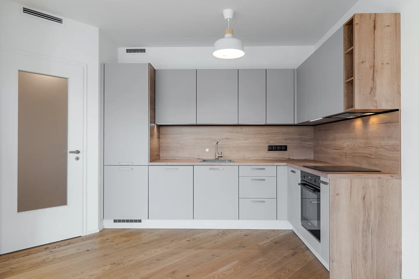 Modern kitchen with gray cabinets, wood countertops, and stainless steel sink. White door and wood floors.