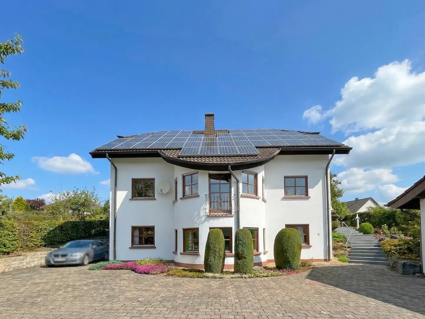A two-story white house with solar panels on the roof under a blue sky.