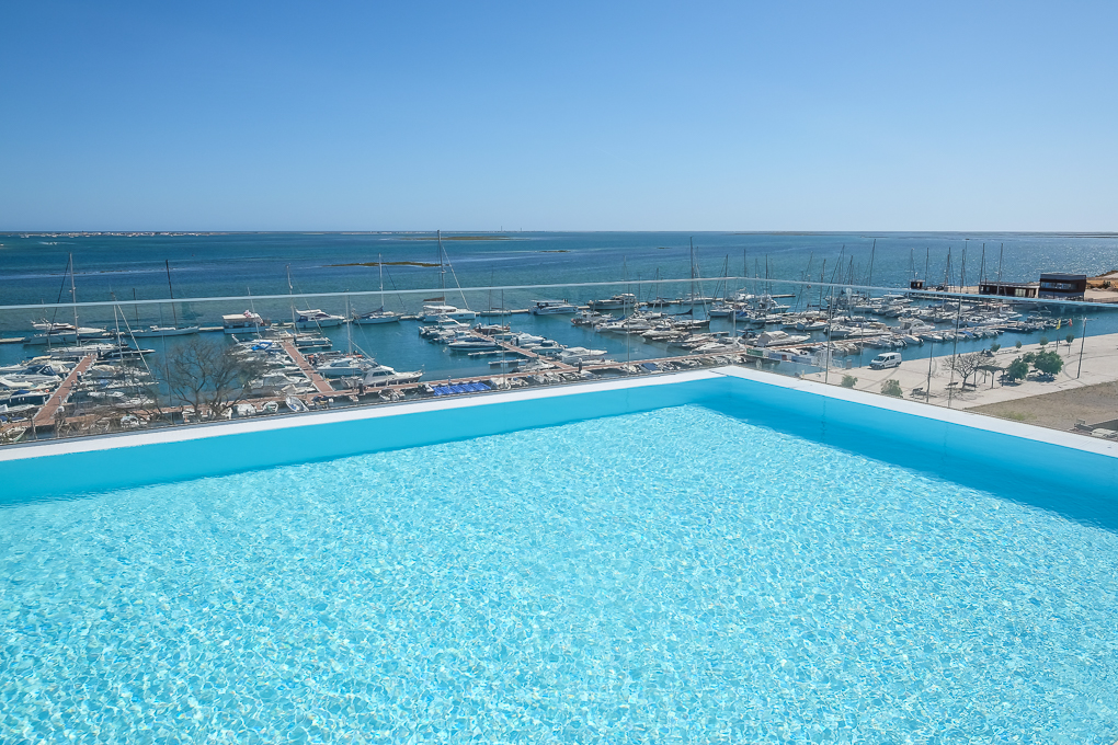 Infinity pool with bright blue water overlooking a marina filled with boats under a clear blue sky.