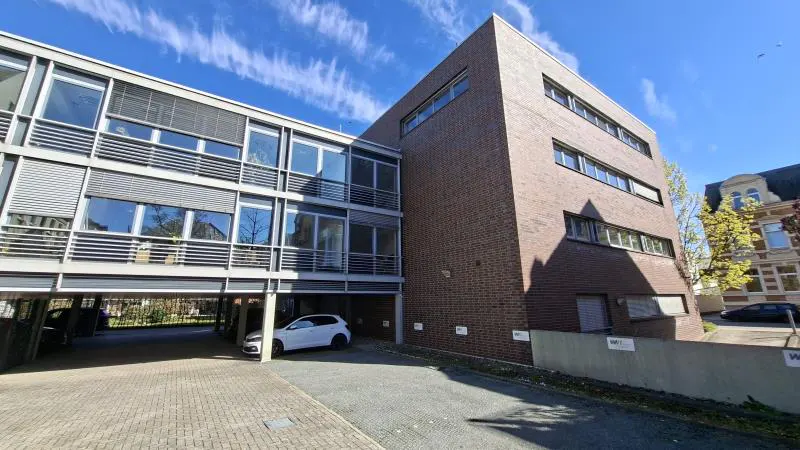 Exterior view of a modern office building with brick and glass facade, parking area, and blue sky.