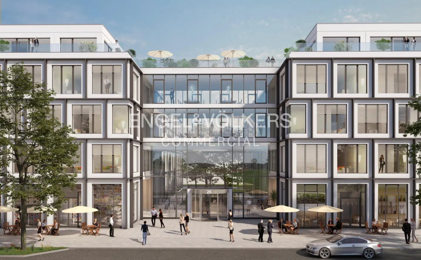 Modern commercial building with glass facade, Engel & Volkers signage, outdoor seating, and people walking.