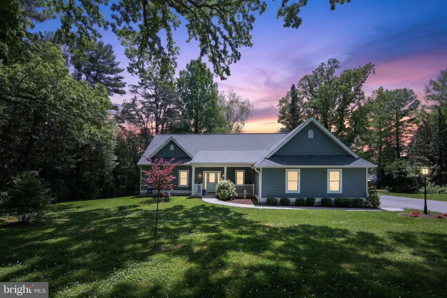 Exterior view of a one-story blue house with a gray roof, white trim, and a green lawn at dusk.