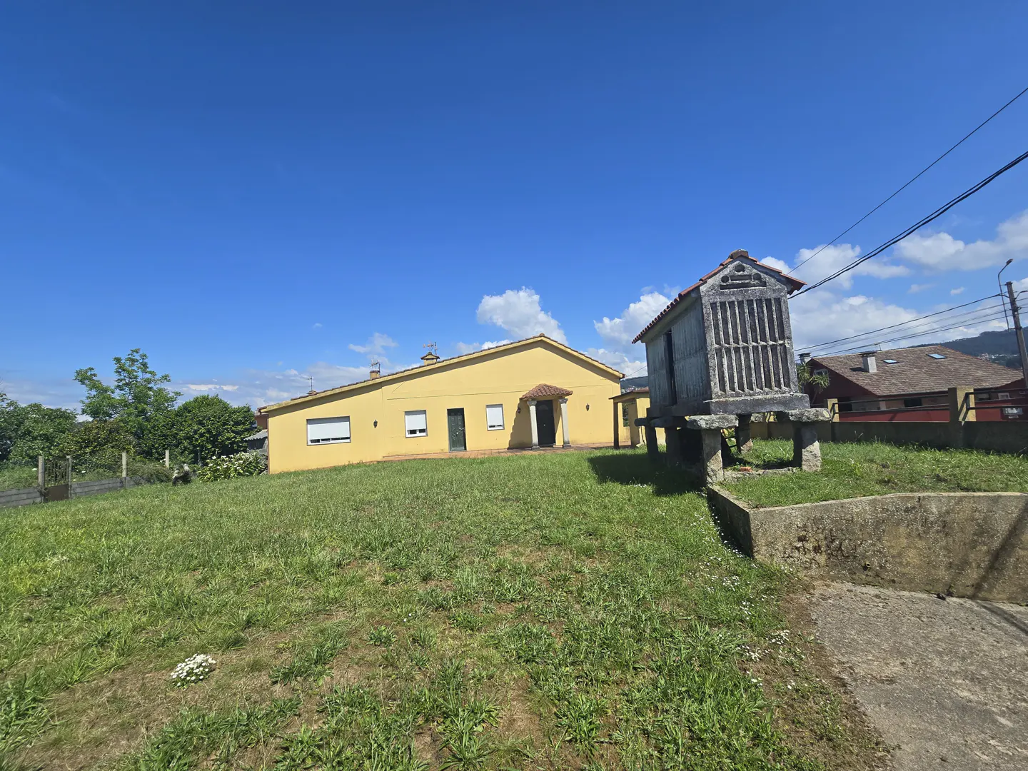 Exterior view of a yellow house with a traditional Galician granary (hórreo) on a sunny day.