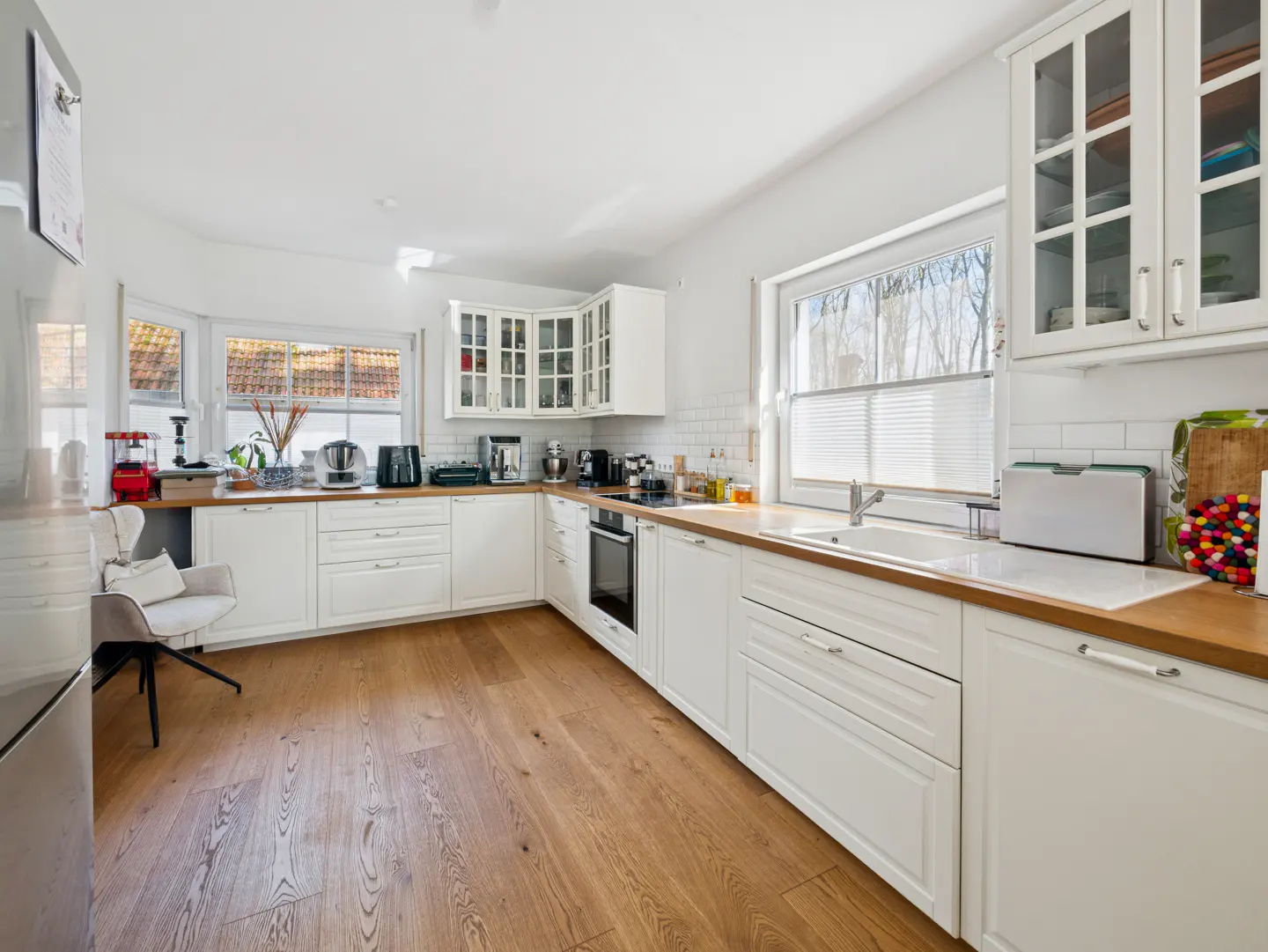 Bright kitchen with white cabinets, wood countertops, and wood floors. A window with blinds is above the sink. Appliances are on the counter.