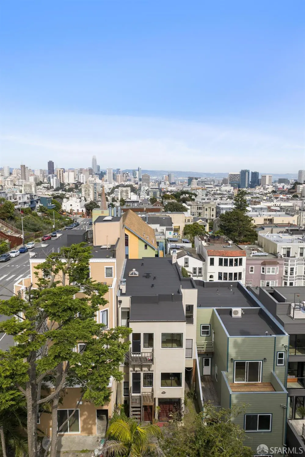 San Francisco cityscape view from above, featuring colorful houses, green trees, and a clear blue sky.