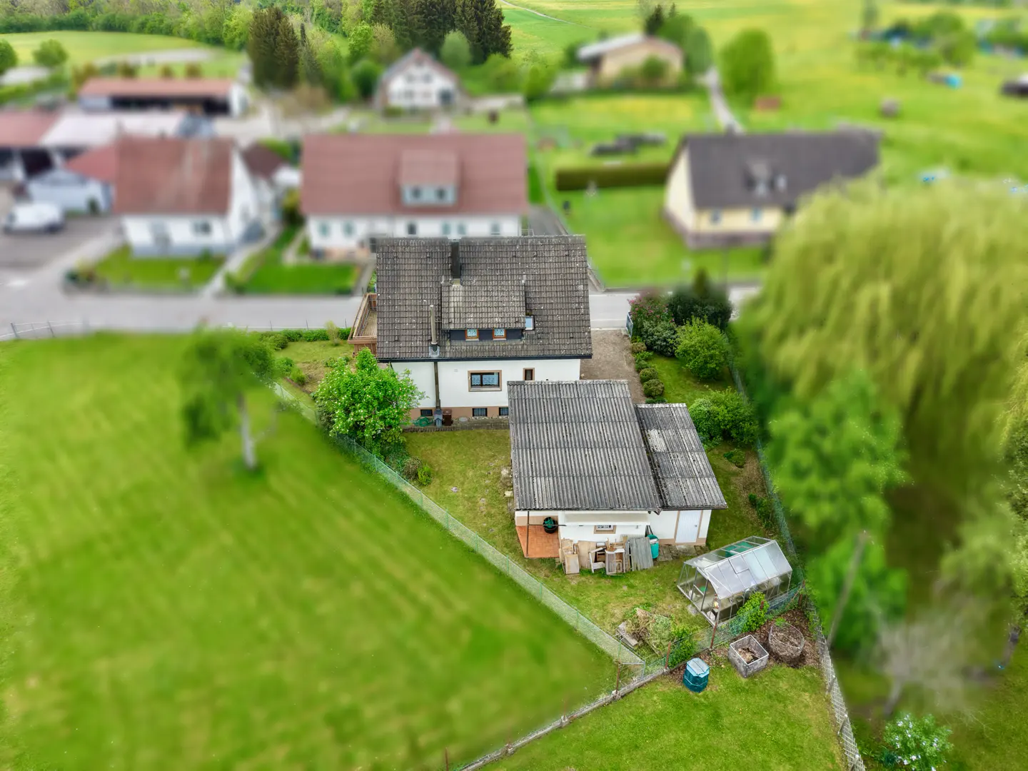 Aerial view of a white house with a gray roof, surrounded by a green lawn, trees, and other houses in the background.
