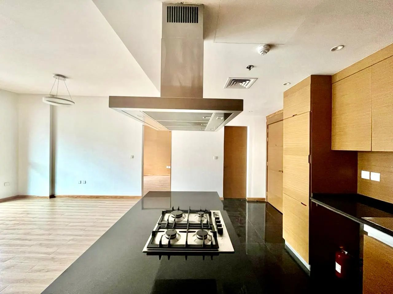 A modern kitchen with a black countertop island, stainless steel range hood, and light wood cabinets.