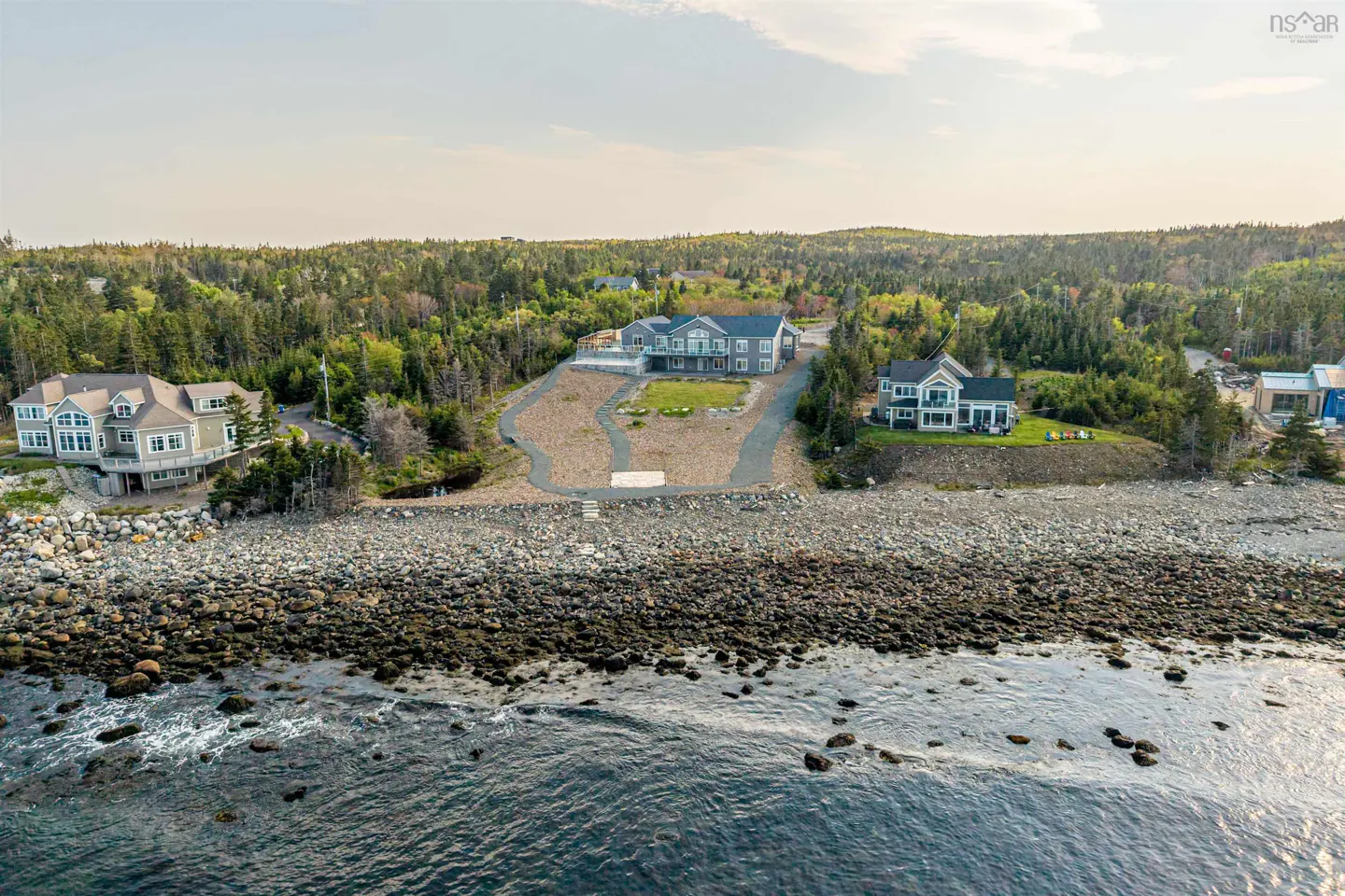 Aerial view of three coastal homes nestled in a lush forest along a rocky shoreline overlooking the ocean.