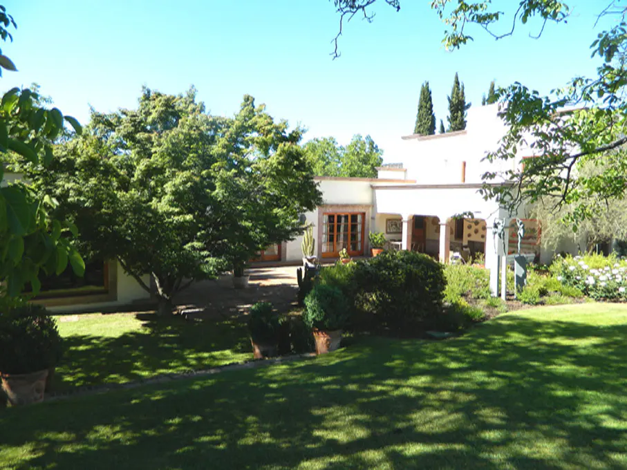 Exterior view of a white stucco house with a green lawn and trees under a blue sky.