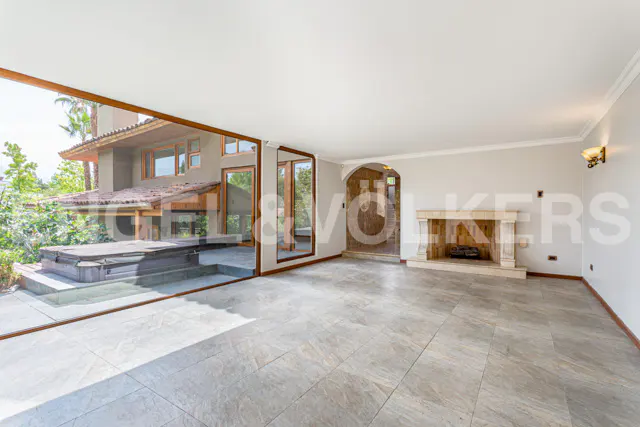 Spacious room with gray tile floors, a stone fireplace, and a large glass wall overlooking a patio with a hot tub.