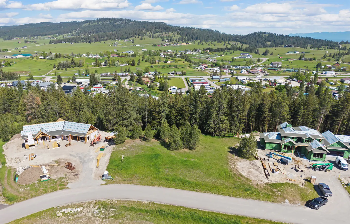 Aerial view of two houses under construction, surrounded by green trees and a town in the background.