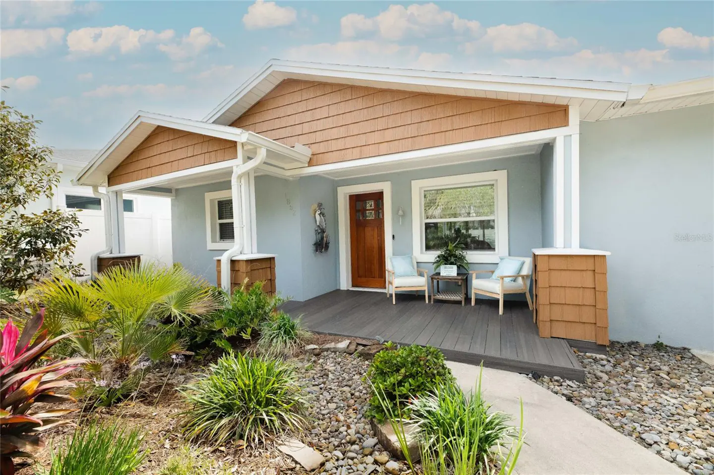 Exterior of a light blue house with a brown door and porch with two chairs.