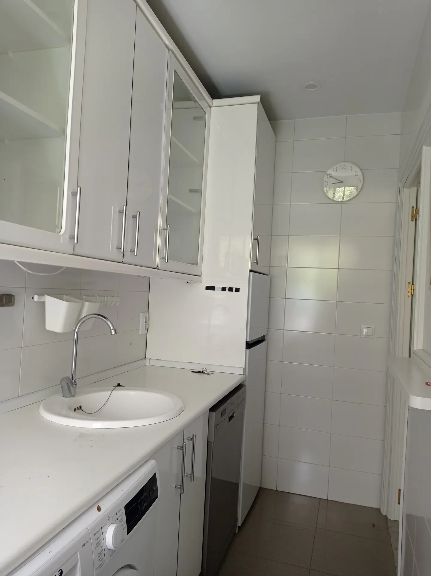 A bright kitchen with white cabinets, countertops, and appliances. A sink with a faucet is visible, along with a washing machine and dishwasher.