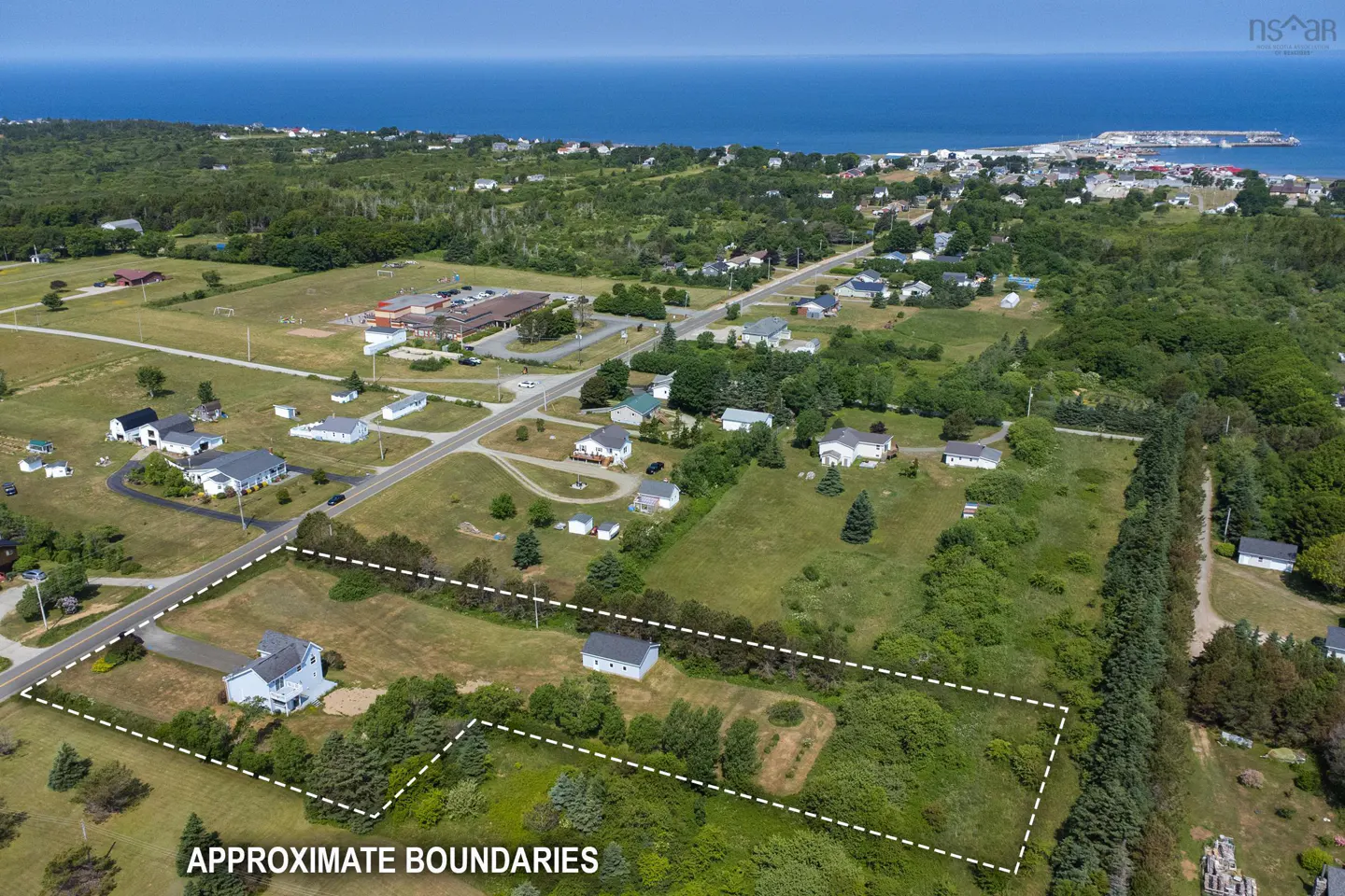 Aerial view of a property outlined in white, with houses, trees, and the ocean in the background.