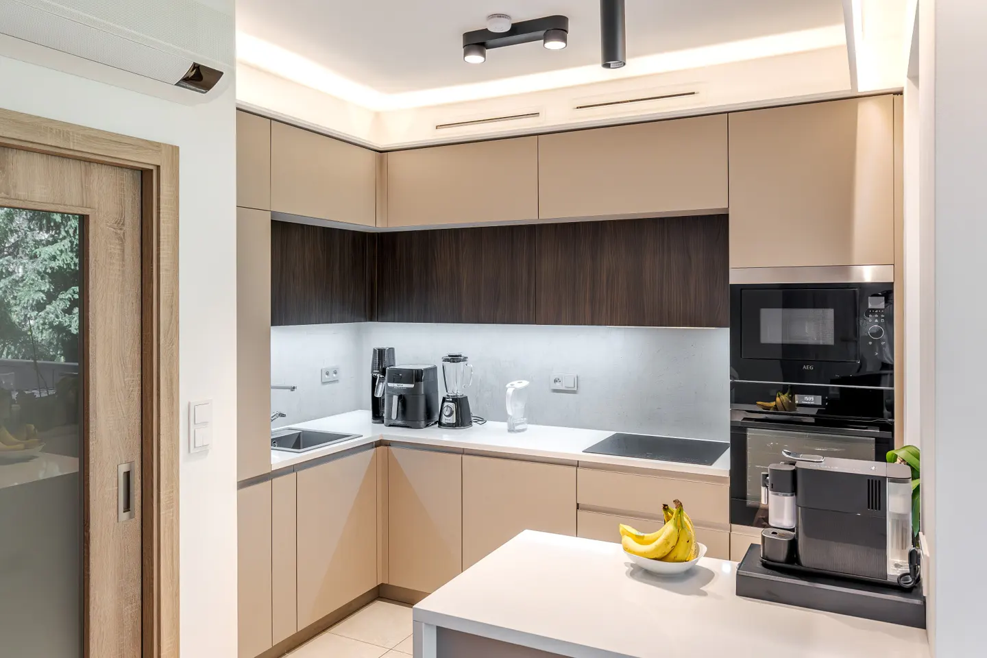 Modern kitchen with beige cabinets, dark wood backsplash, white countertops, built-in appliances, and a bowl of bananas.