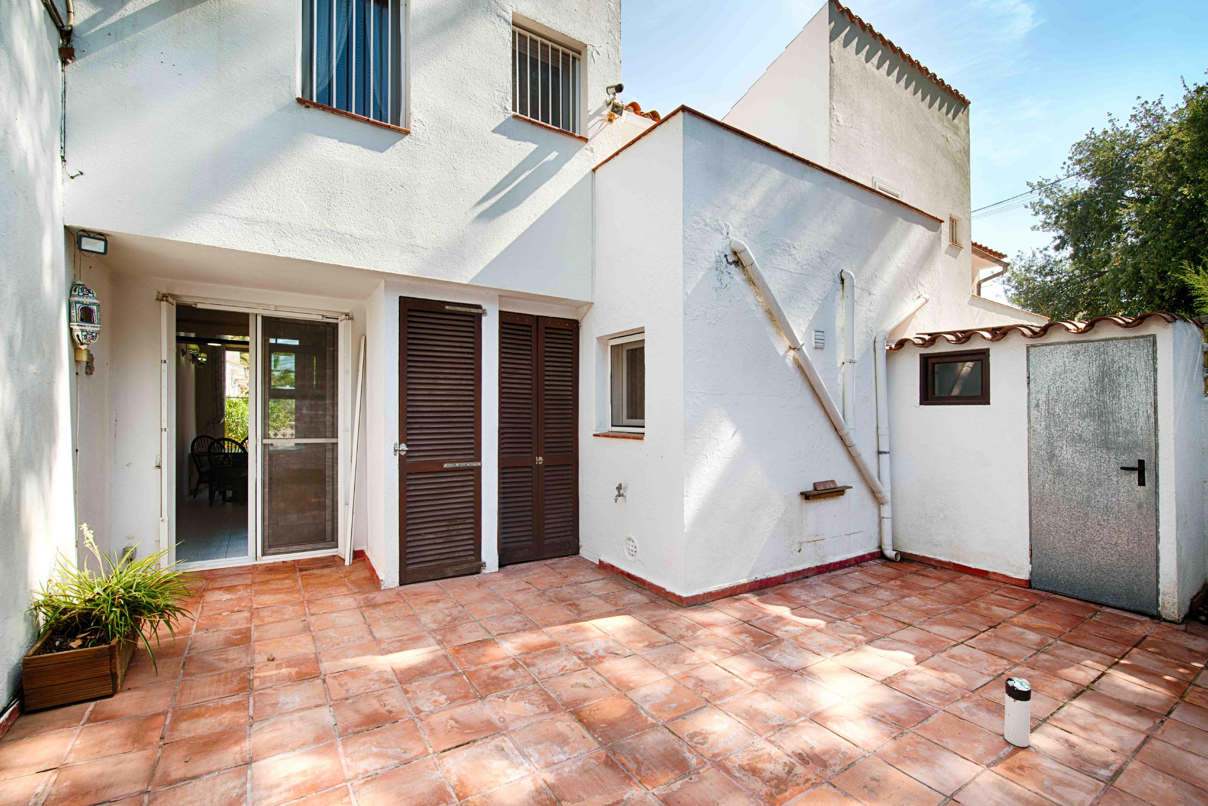 Exterior view of a white building with a terracotta tiled patio, brown shutters, and a sliding glass door.