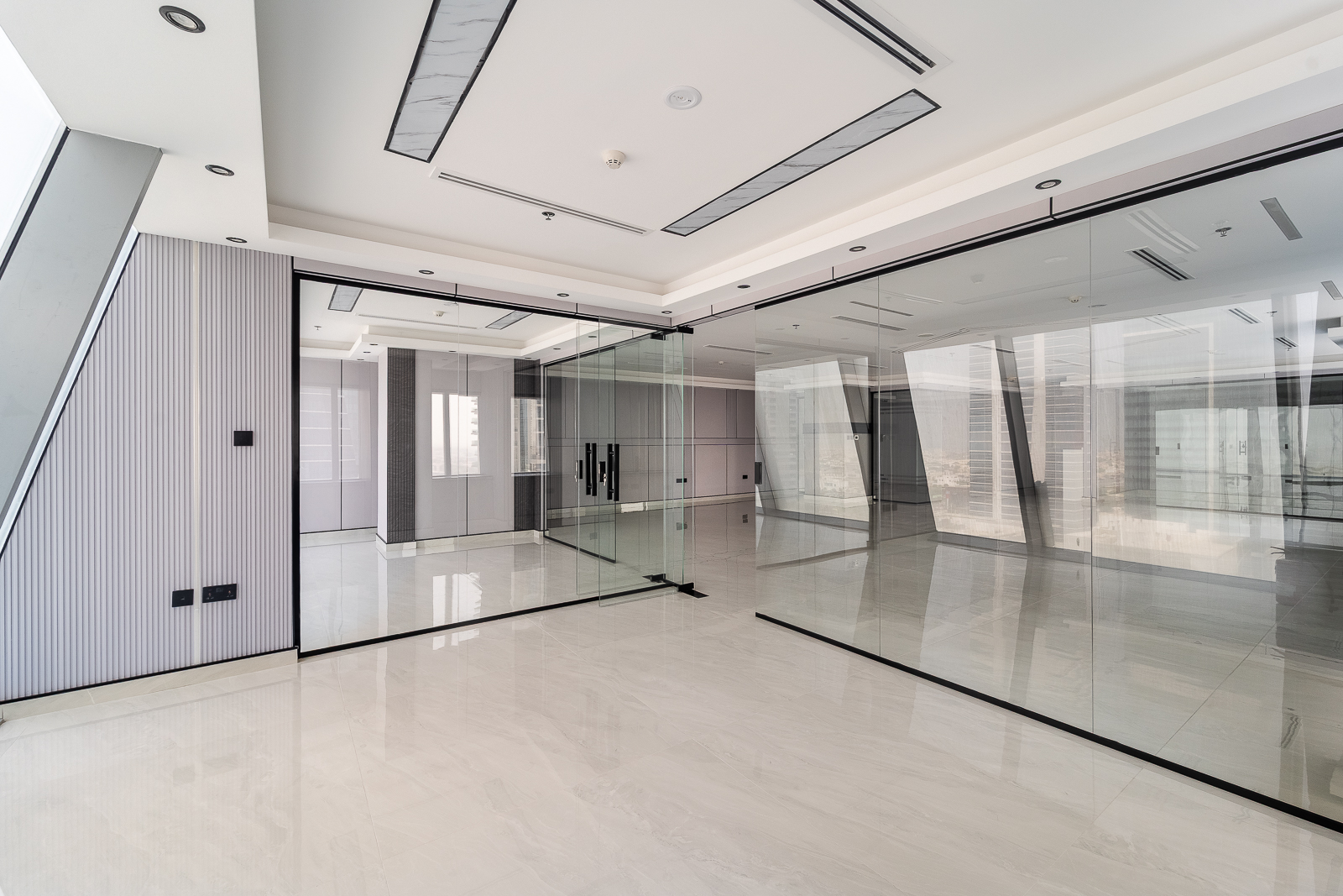 Modern, empty office space with white marble floors, glass partitions, and recessed ceiling lighting. [AI-generated text]