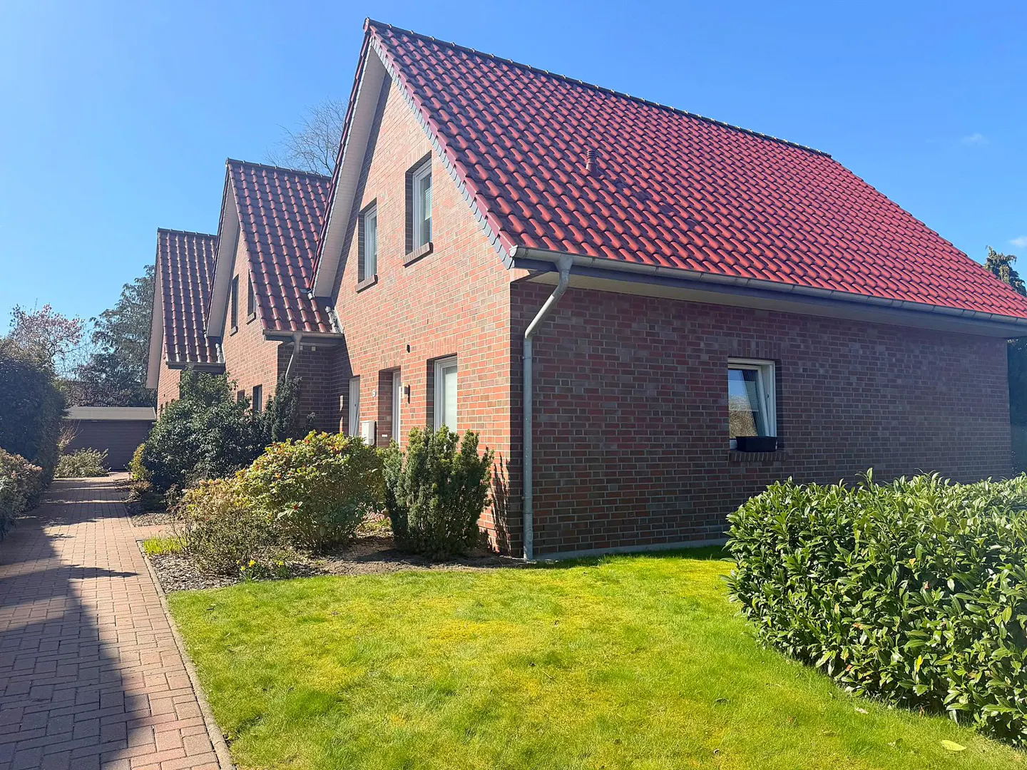 Row of brick houses with red tile roofs, green lawns, and a brick walkway on a sunny day.