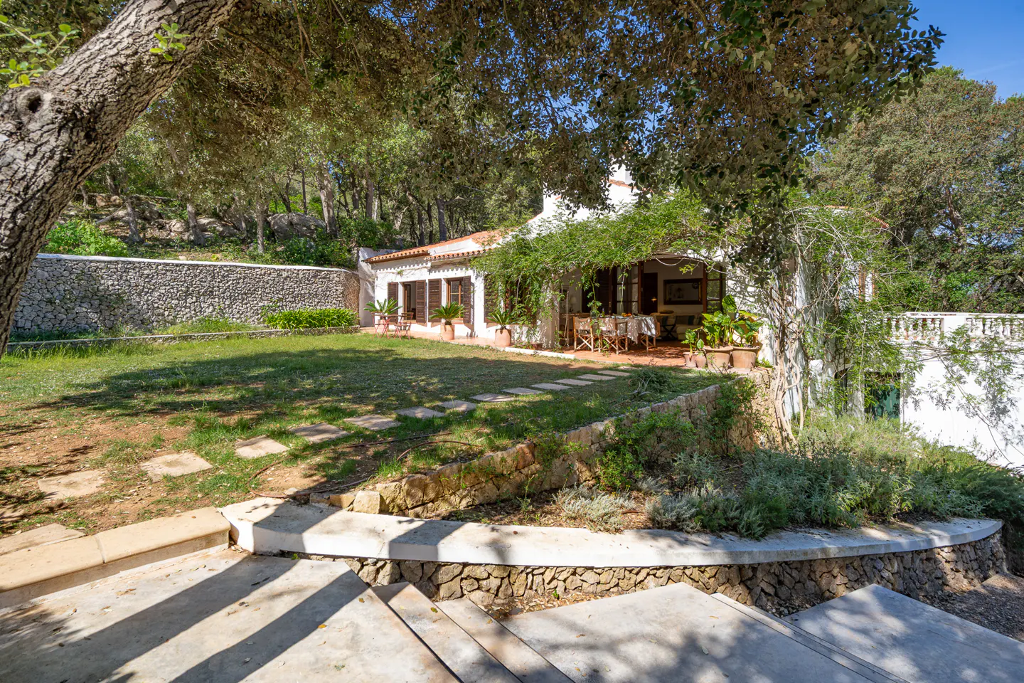 Exterior view of a white house with a red tile roof, a green lawn, and stone steps leading up to the house.