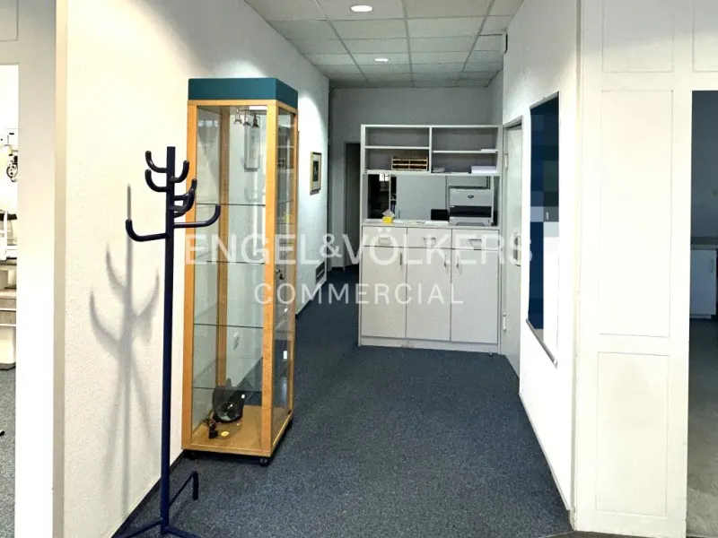 Office hallway with blue carpet, white walls, coat rack, display case, and white cabinets with a printer.