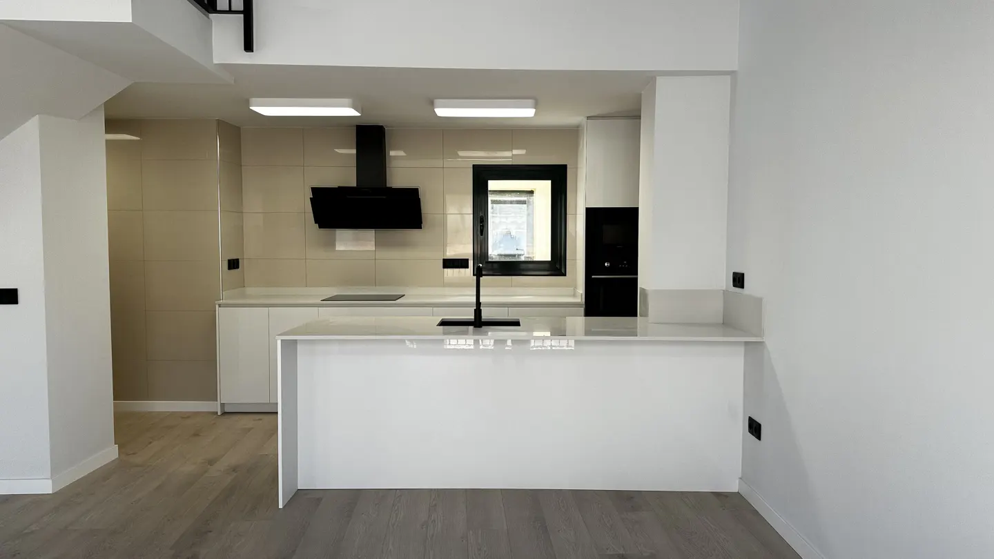 A modern kitchen with white cabinets, a black range hood, and a breakfast bar. The floor is light gray wood.