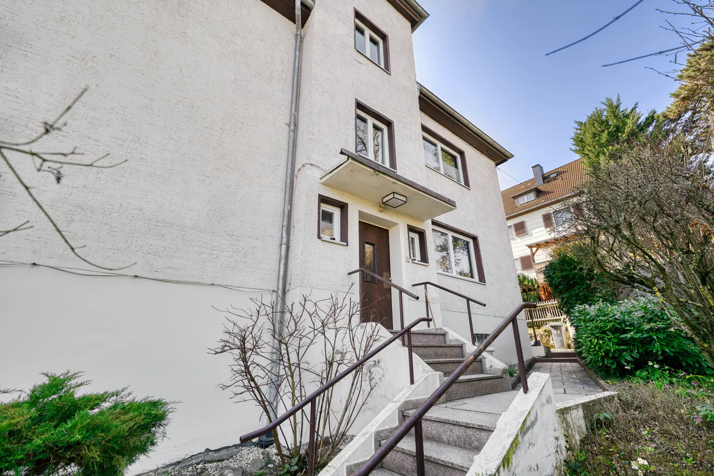 Exterior view of a three-story white building with brown trim, stairs lead to the front door.