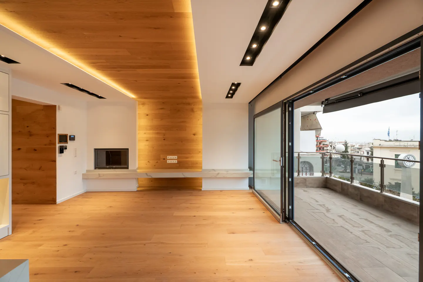 Bright, modern living room with wood floors, a fireplace, and sliding glass doors to a balcony overlooking a city.