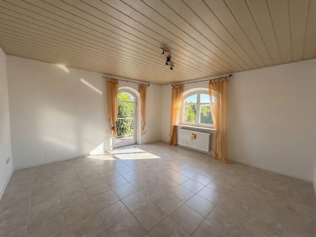 Empty room with tile floor, white walls, and wood-paneled ceiling. Arched windows with sheer orange curtains let in sunlight.