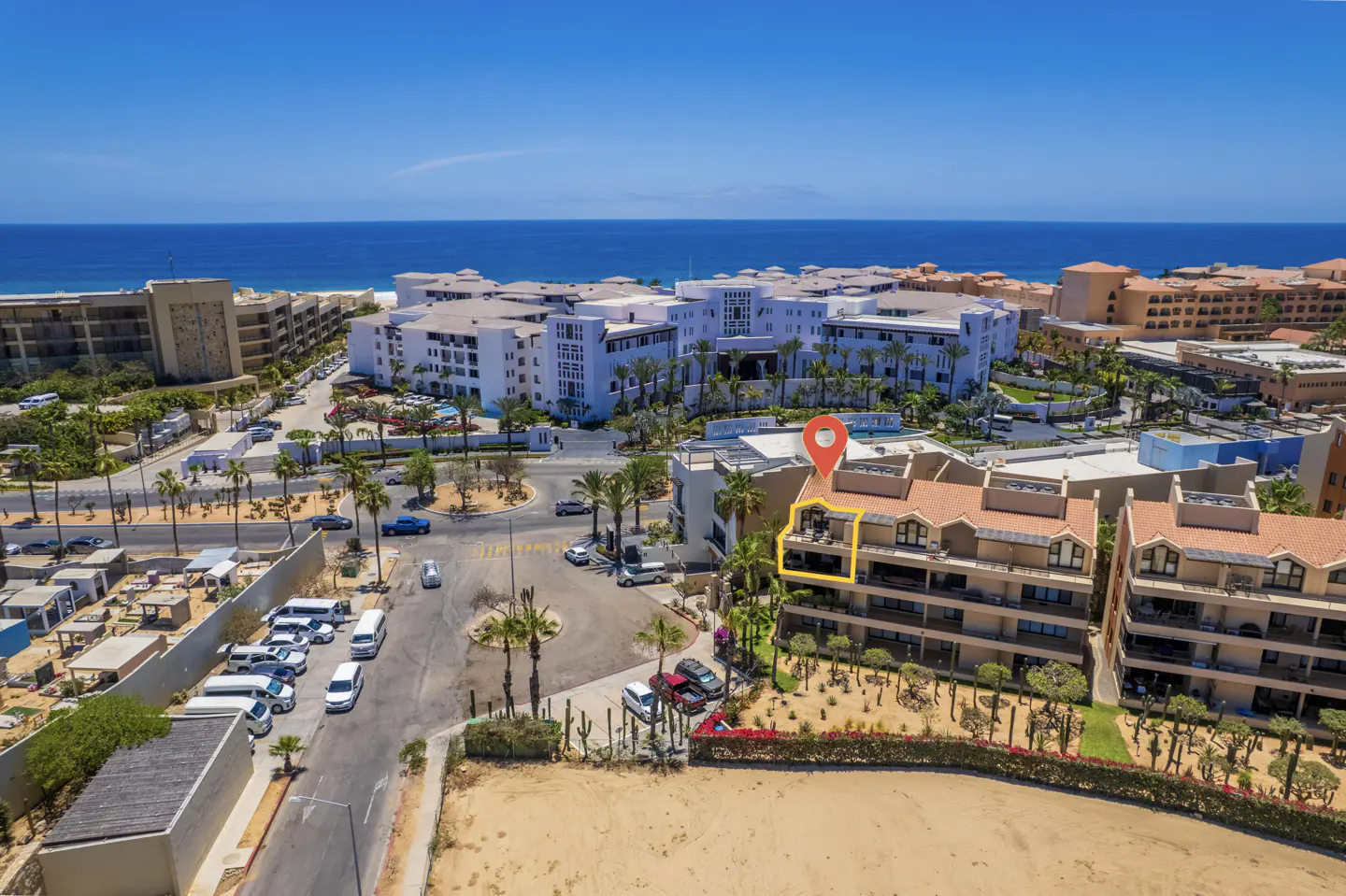Aerial view of a condo with a red location pin, near the ocean and other buildings, under a blue sky.