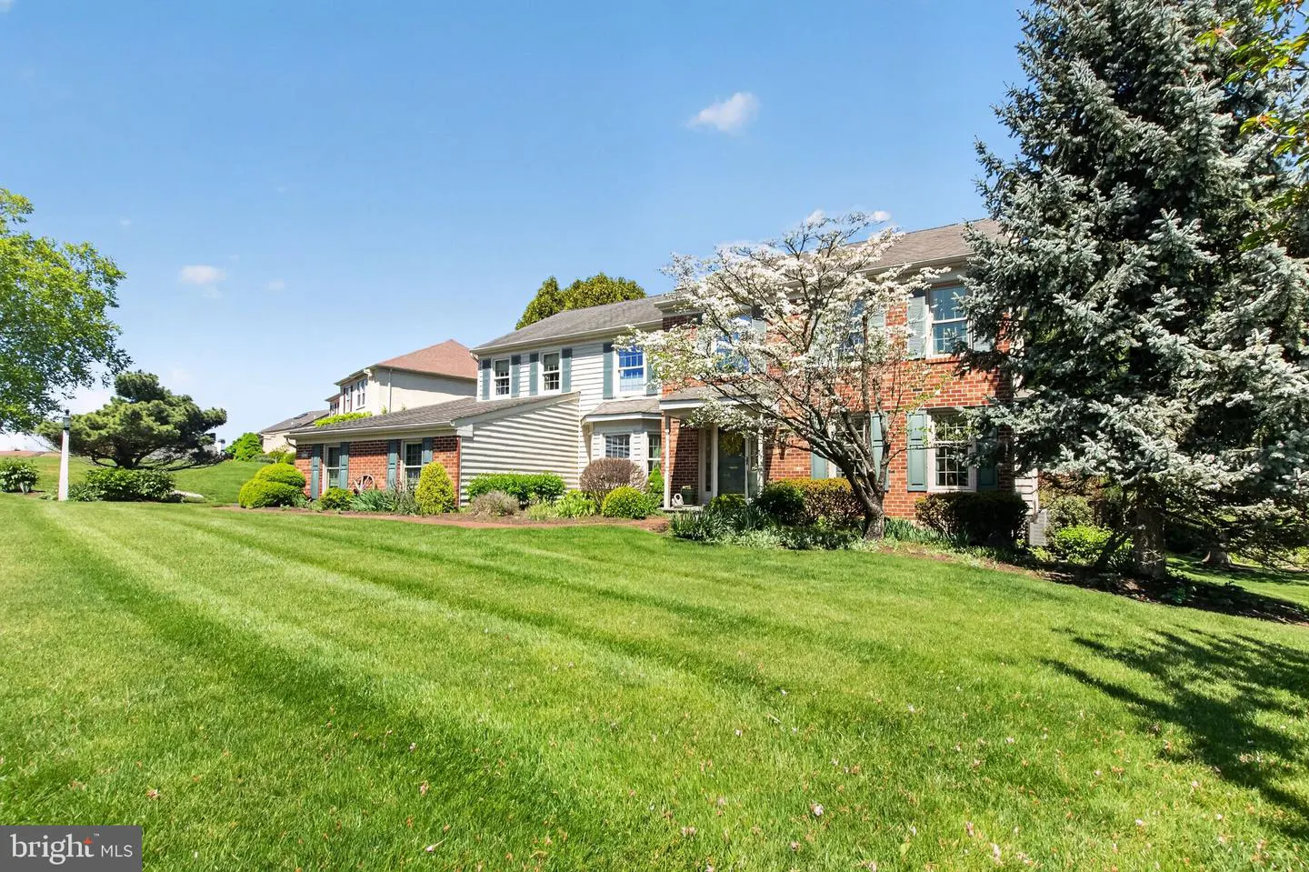 Two-story house with brick and siding, green shutters, and a large lawn under a blue sky.
