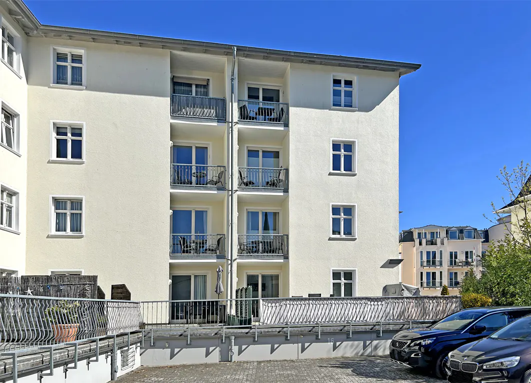 Exterior of a cream-colored apartment building with balconies and parked cars under a clear blue sky.