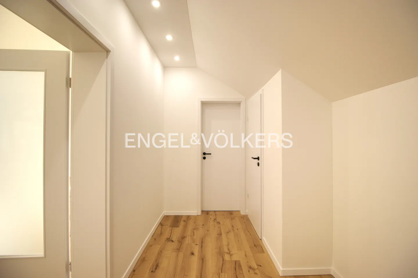 Bright hallway with wood floors, white walls, and two closed white doors. Engel & Völkers logo is visible.
