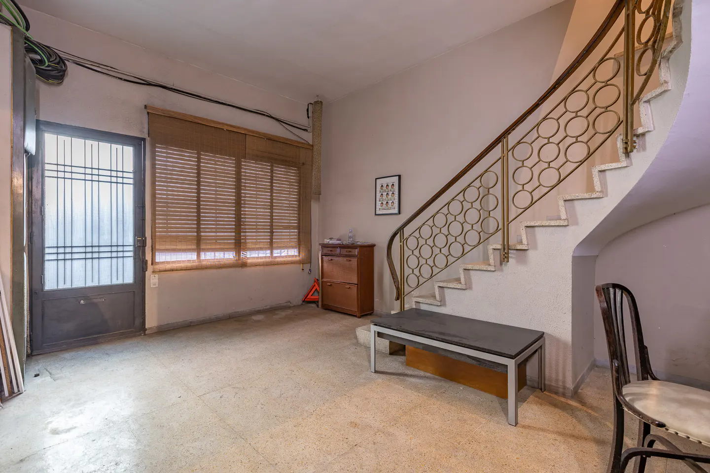 Entryway with a metal-railed staircase, a wooden cabinet, a bench, a window with blinds, and a glass-paneled door.
