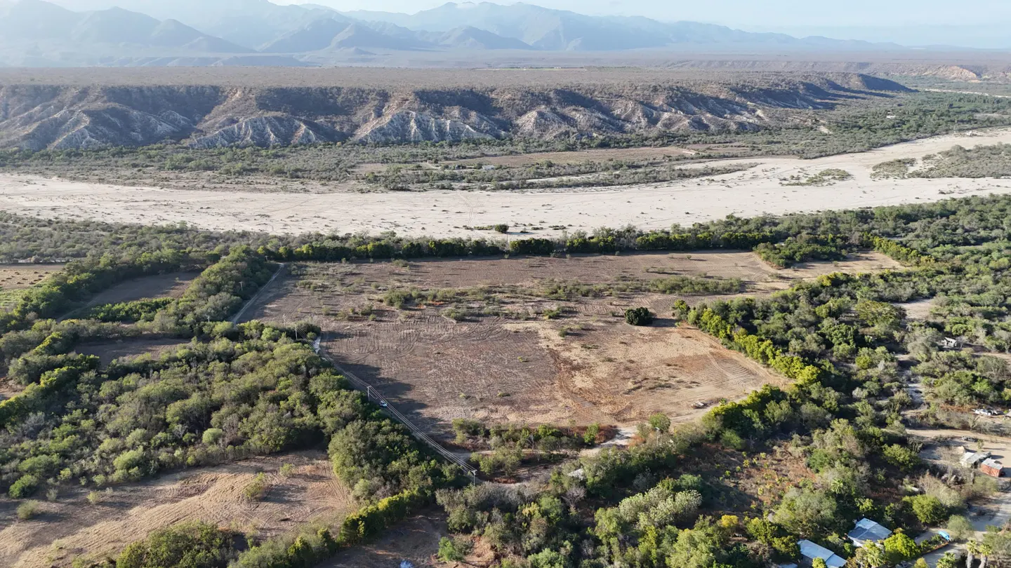 Aerial view of a rural landscape with dry fields, green trees, and mountains in the background.