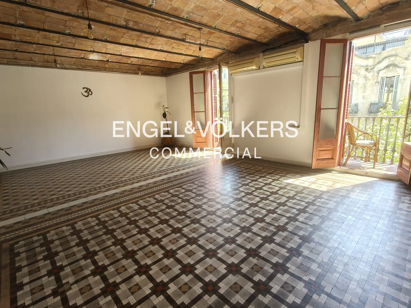 A bright, empty room with patterned tile floors and a balcony with a wicker chair.