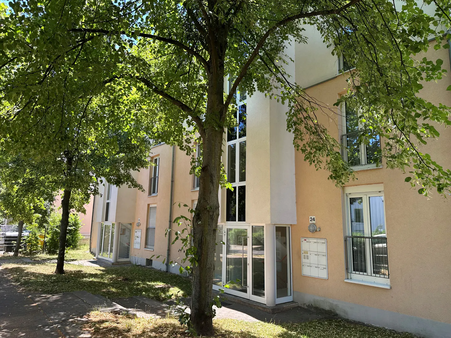 Exterior view of a peach-colored apartment building with green trees in the foreground. The building has white trim and large windows.