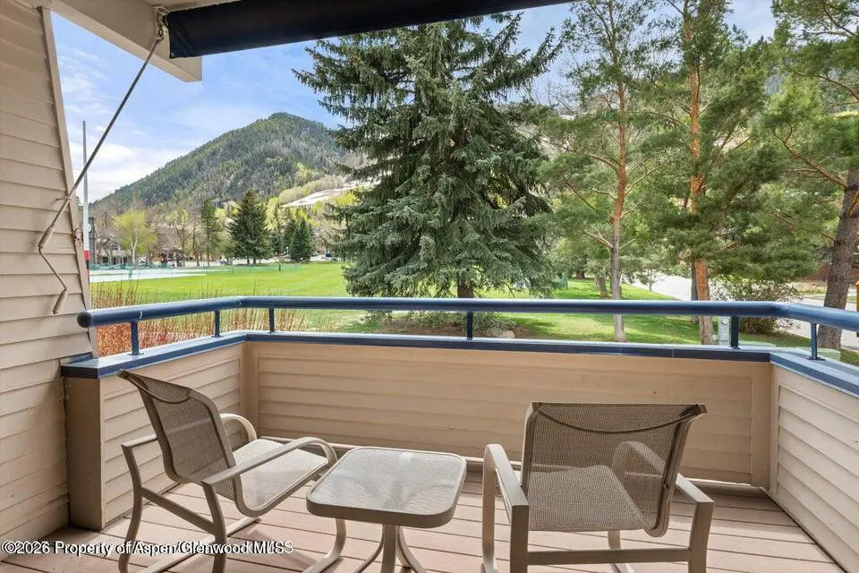 Balcony view with two chairs and a table overlooking a green lawn and mountain.