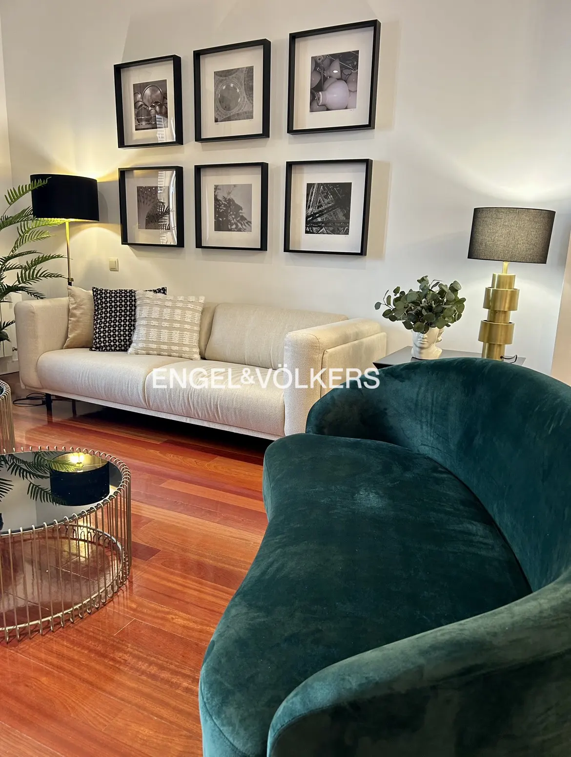 Living room with a cream sofa, green velvet chair, and black and white framed art on the wall.