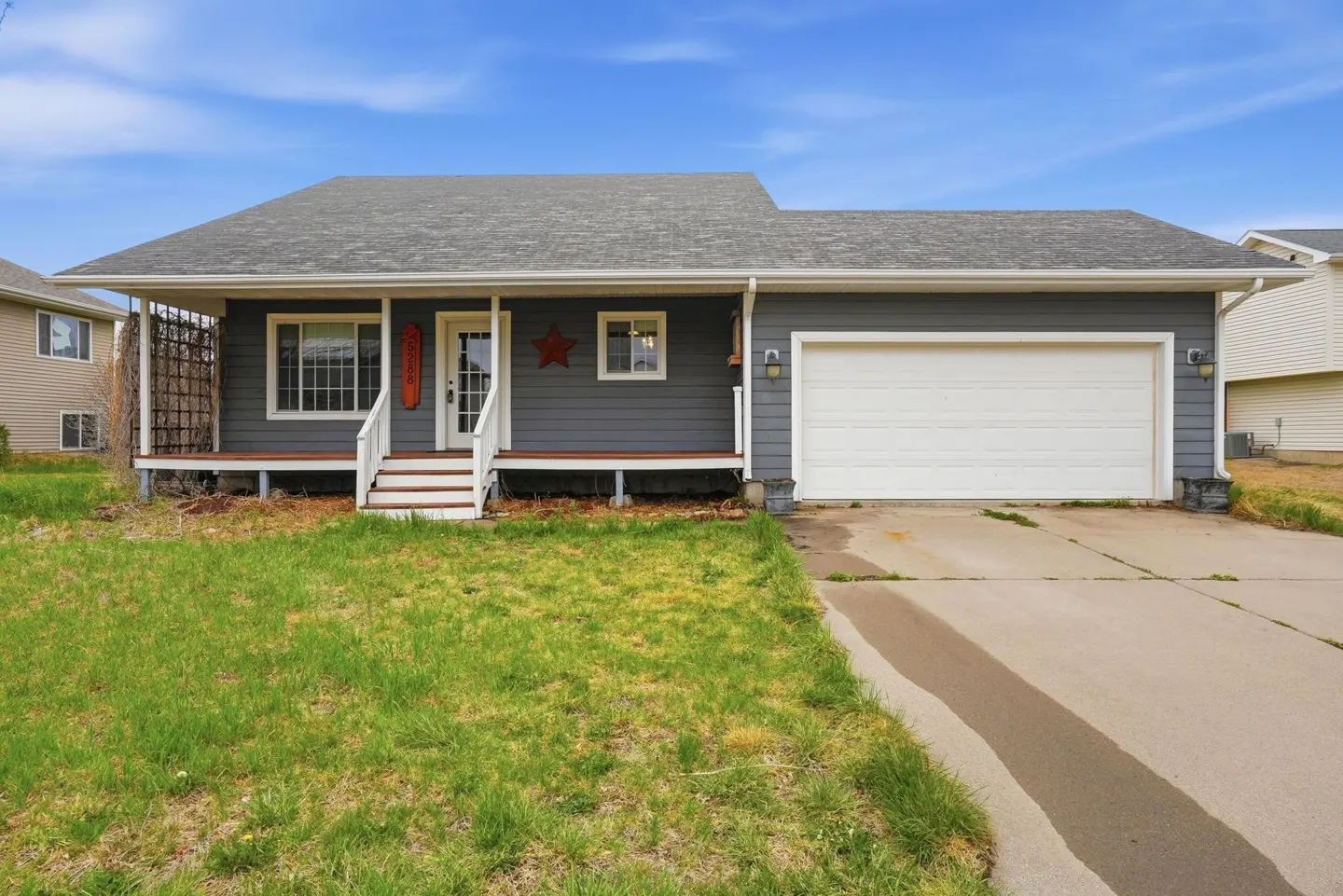 A gray, one-story house with a white garage door and a lawn. The house has a porch with white stairs.
