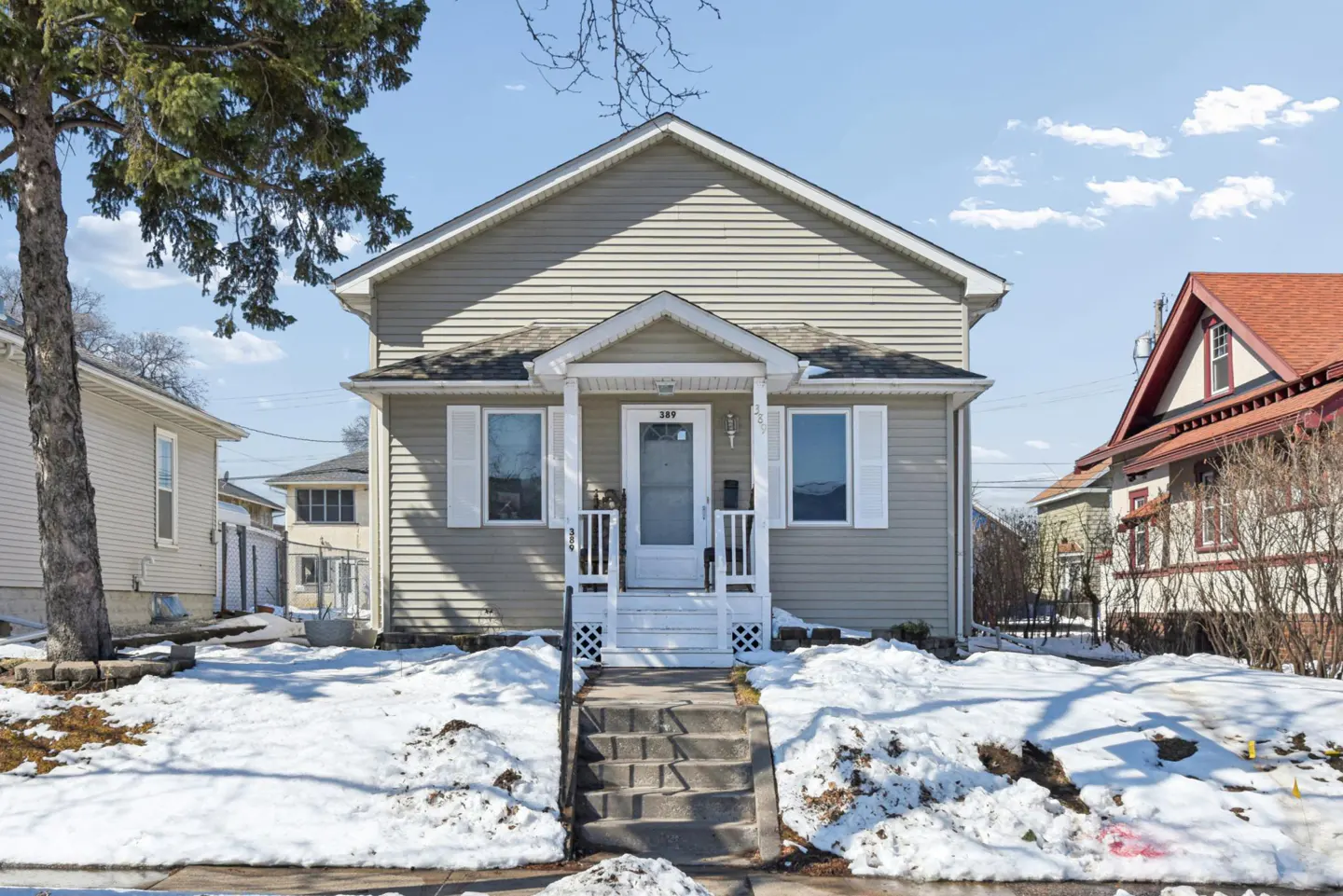 A two-story house with light-green siding, white trim, and a front yard covered in snow.