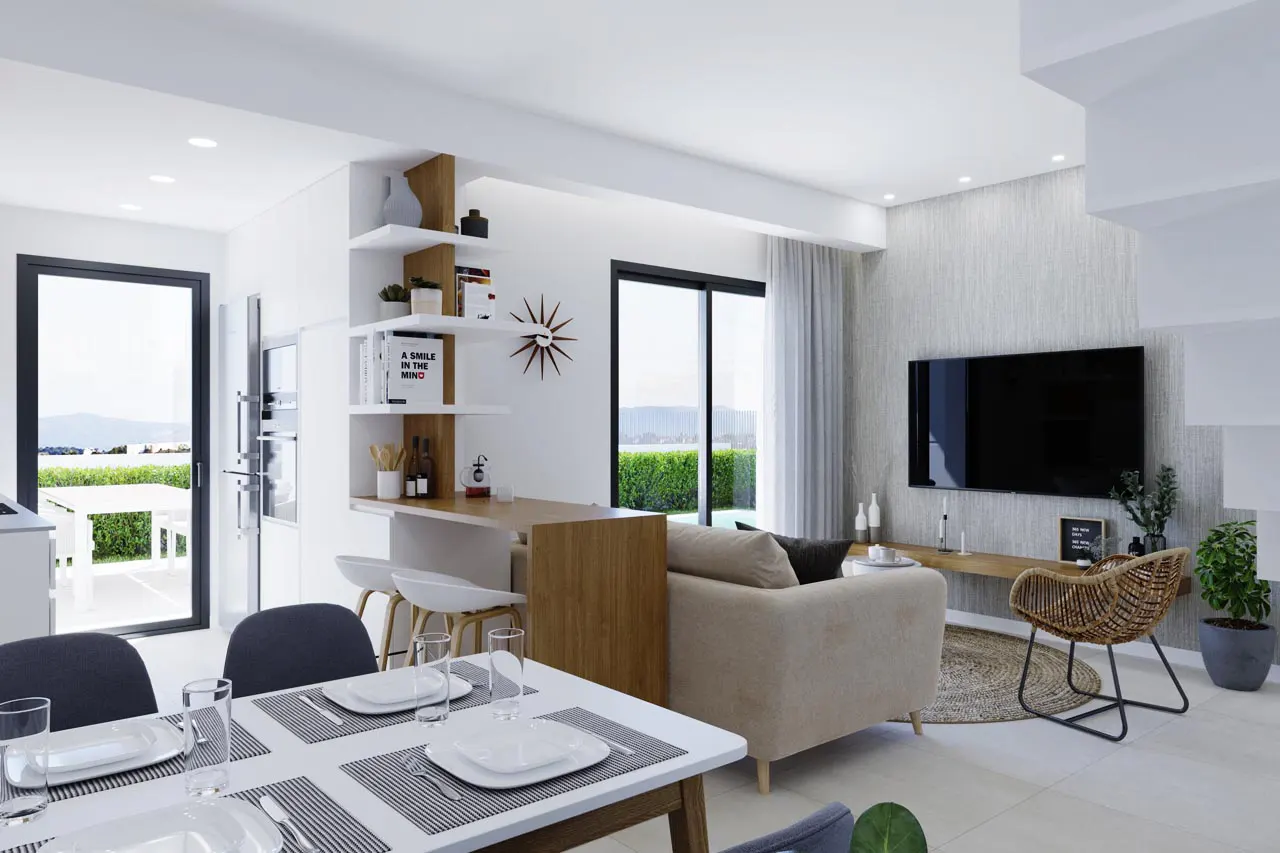 Bright, modern living space with a dining table set for four, a beige sofa, and a TV on the wall. Shelves display books and decor. Outside, greenery is visible.