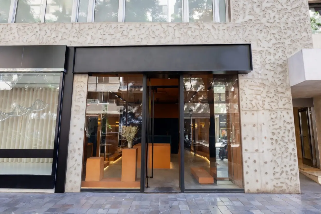 Storefront with glass windows and black trim, showcasing orange displays and wheat stalks inside. Textured beige building facade.